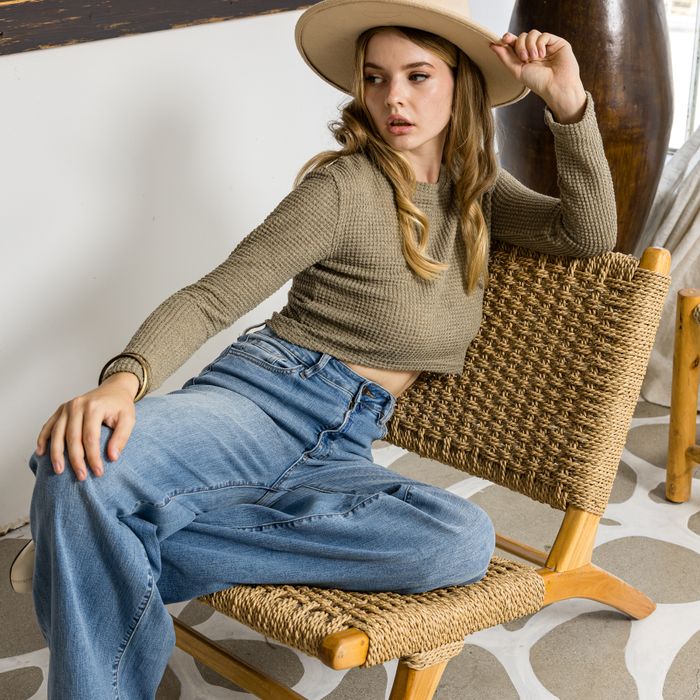 Stylish woman in casual attire posing on a woven chair, showcasing fashion trends.
