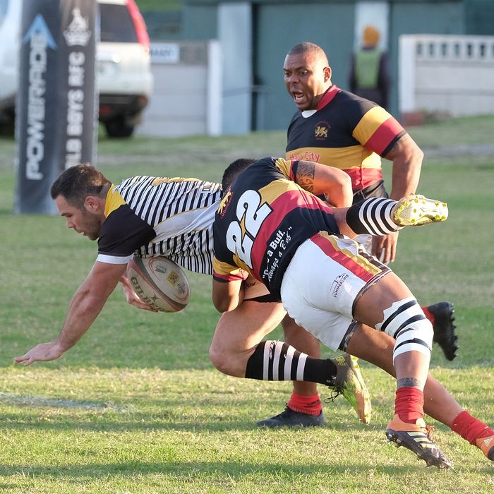 Rugby players tackling on a green field during a match in South Africa, showing athleticism and teamwork.